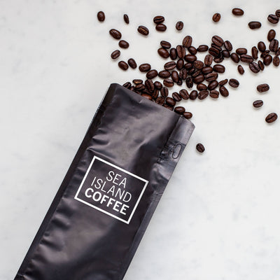Black Sea Island Coffee bag with roasted coffee beans pouring out of it, laying on a marble background