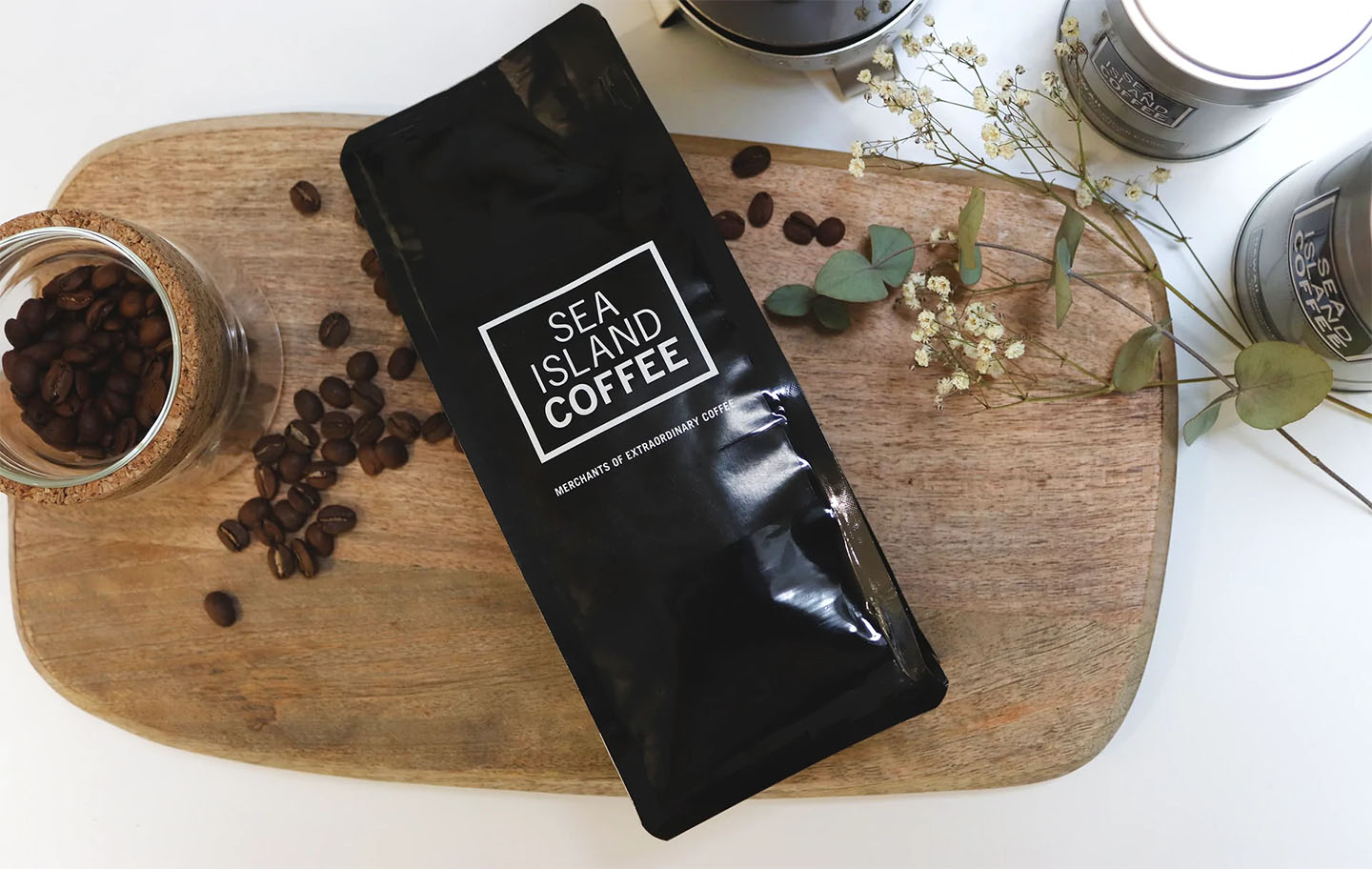 A bag of coffee beans with some flowers, laying across a copping board