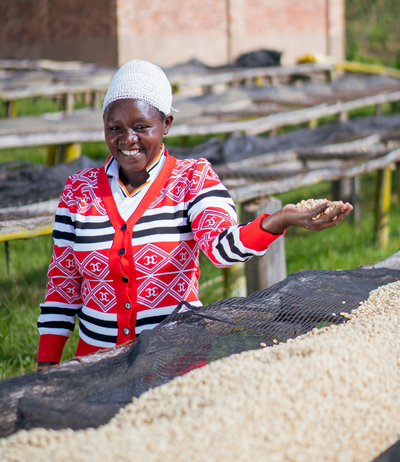 Female coffee farmer in Rwanda smiling while hand-sorting dried coffee beans