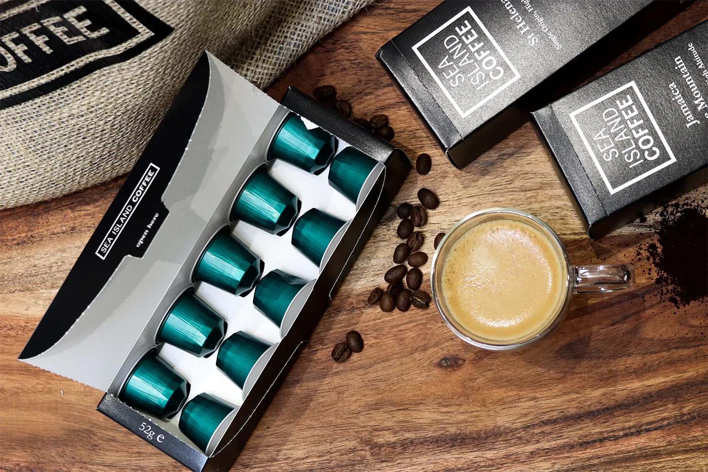 An open box of Nespresso compatible aluminium capsules next to a cup of coffee